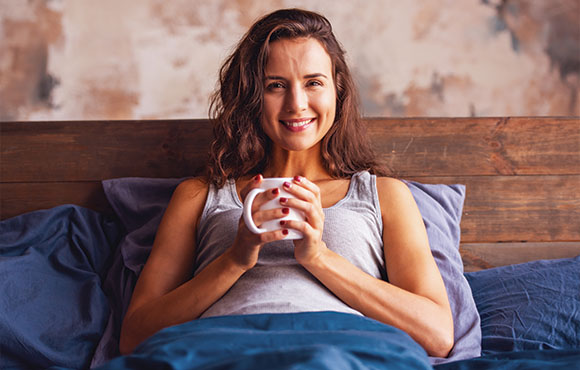 smiling woman holding a mug in bed cozy morning routine relaxation 3 tips for comfort
